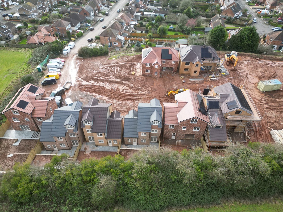Aerial view of the Grange View Road plots mid build, solar panels already fitted across the finished roofs beside the working plots