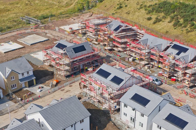An aerial view of a housing site under construction, with houses in scaffolding and their roofs part tiled