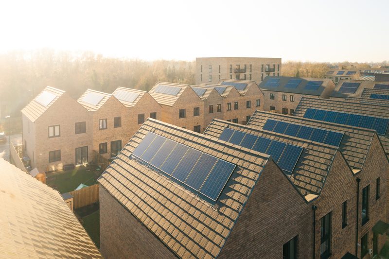 Rows of new build houses with solar panels set into their roof tiles, seen from above in low sun