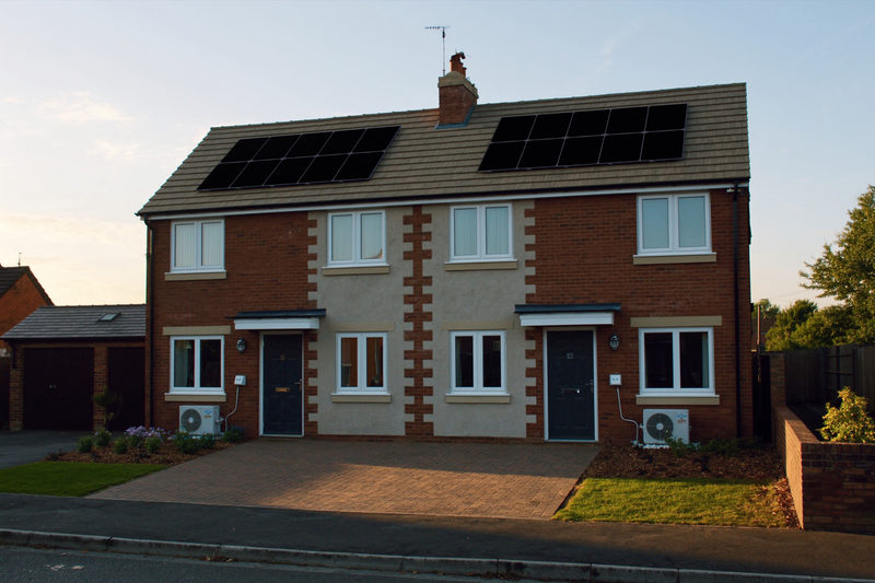 A new build semi detached pair with solar panels on both roof slopes and an air source heat pump beside each front door