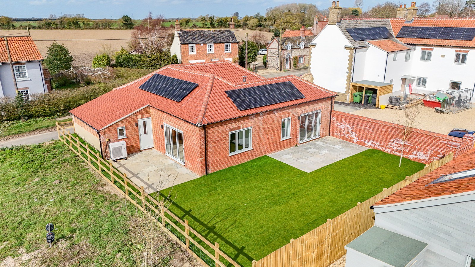 The garden side of a finished Lower Farm Mews plot seen from the air, lawn and patio under panels on the roof